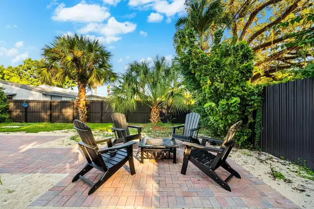 Fenced backyard at Light House with a brick patio, a fire pit, four Adirondack chairs and palm trees