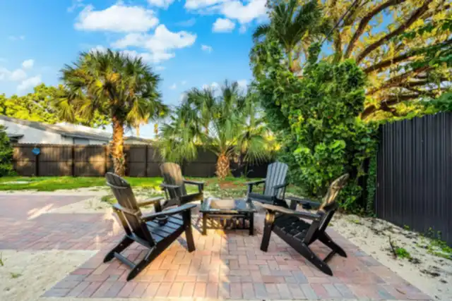 Fenced backyard at Light House with a brick patio, a fire pit, four Adirondack chairs and palm trees
