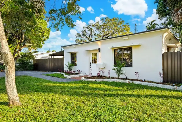 Front of Light House: a white single-storey house with a lawn, planted beds and a shade tree
