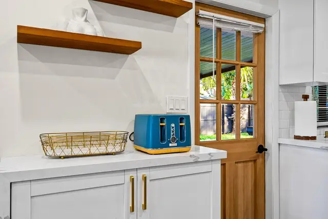 Kitchen counter at Light House with a blue toaster, floating wooden shelves and a glass-panel door