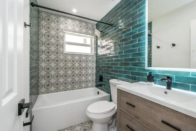 Bathroom at The Gulch with a bathtub, patterned and teal wall tiles, and a backlit mirror over the vanity