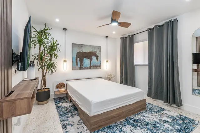 Bedroom at The Gulch with a platform bed, wall-mounted TV, pendant lights, an indoor plant and a blue rug