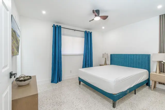Bedroom at The Gulch with a teal upholstered bed, blue curtains, bedside lamps and a ceiling fan