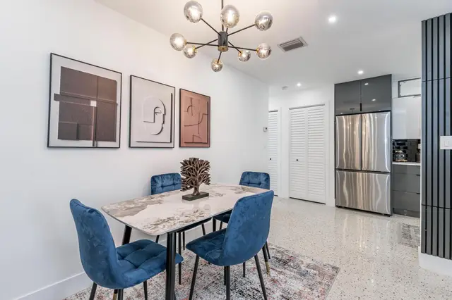 Dining table at The Gulch with four blue velvet chairs, with the stainless steel refrigerator behind