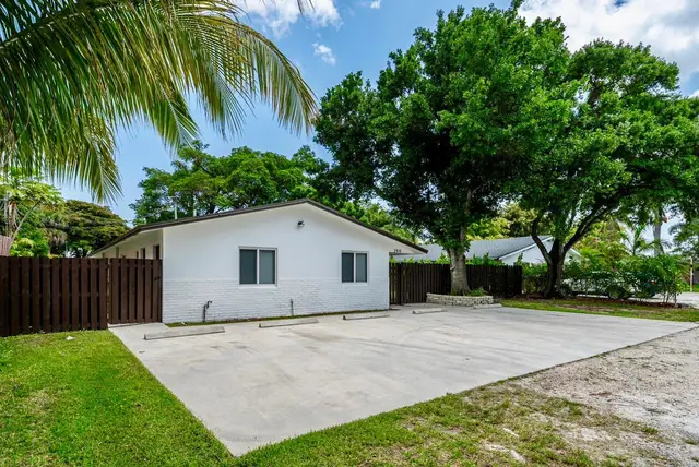 Outside The Gulch: a white single-storey building with a paved parking area, palm tree and fence