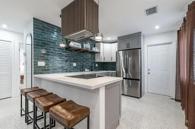 Kitchen at The Gulch with an island and four leather bar stools, a teal tiled wall and a stainless steel refrigerator